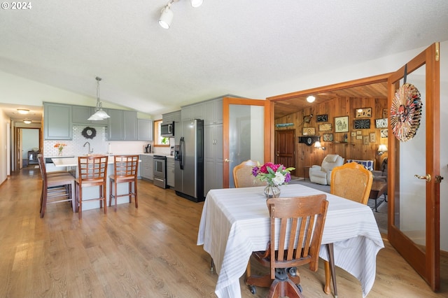 dining space with sink, light wood-type flooring, a textured ceiling, wood walls, and lofted ceiling