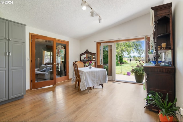 dining space featuring a textured ceiling, light hardwood / wood-style flooring, lofted ceiling, and french doors