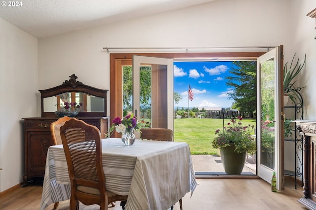 dining space with light wood-type flooring, vaulted ceiling, and a textured ceiling