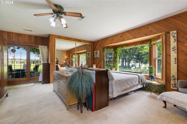 bedroom with a textured ceiling, wooden walls, light carpet, access to outside, and ceiling fan