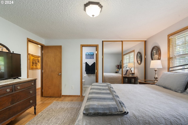 bedroom with light hardwood / wood-style floors, a textured ceiling, a closet, and ensuite bath