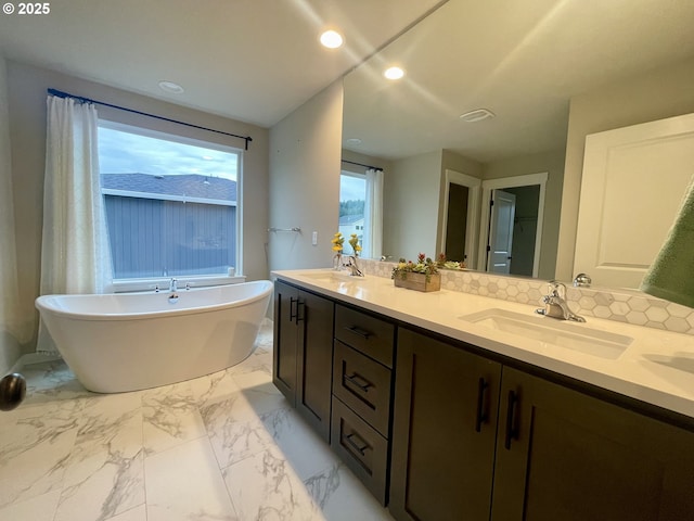 full bath with a soaking tub, double vanity, marble finish floor, and a sink