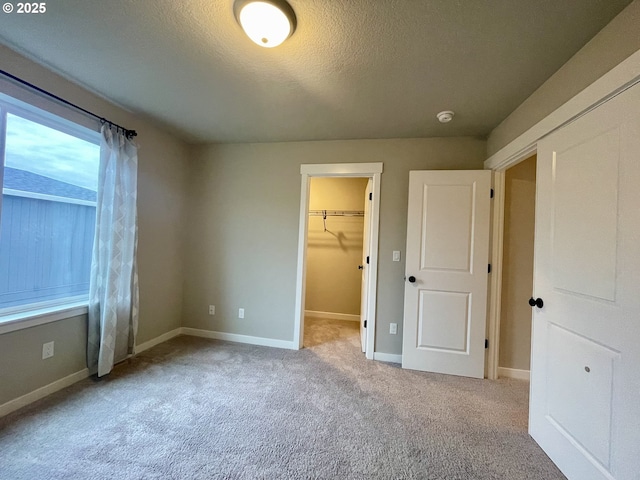 unfurnished bedroom featuring a spacious closet, baseboards, carpet floors, and a textured ceiling