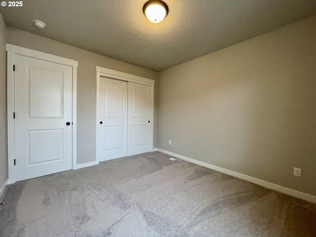 unfurnished bedroom with a closet, carpet flooring, a textured ceiling, and baseboards