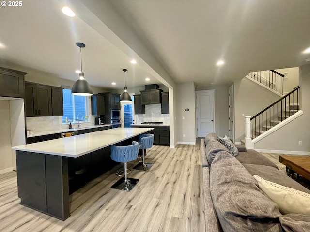 kitchen featuring a spacious island, light wood finished floors, backsplash, open floor plan, and light countertops