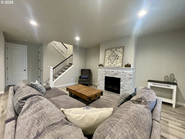 living area featuring wood finished floors, recessed lighting, a stone fireplace, baseboards, and stairs