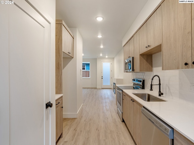 kitchen with light brown cabinets, stainless steel appliances, tasteful backsplash, sink, and light wood-type flooring