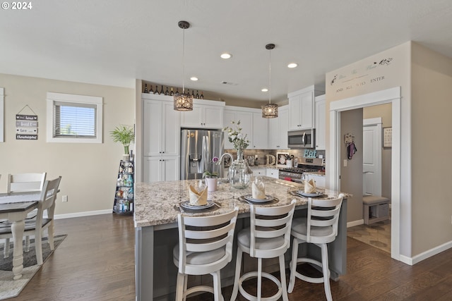 kitchen featuring pendant lighting, white cabinetry, stainless steel appliances, light stone counters, and a center island with sink