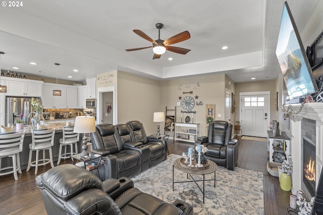 living room featuring dark wood-type flooring, ceiling fan, and a raised ceiling