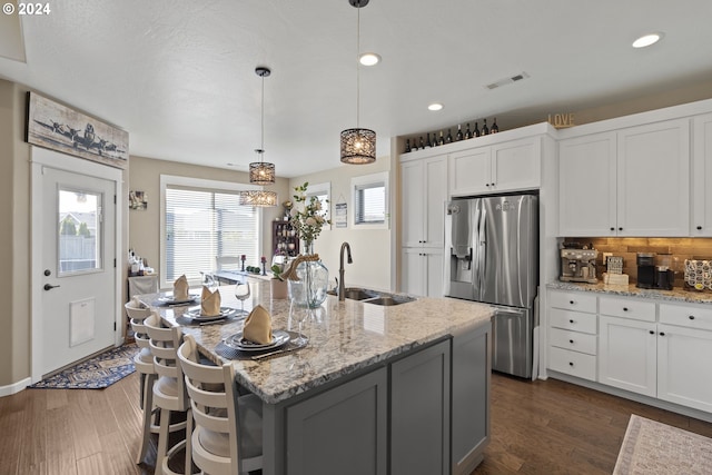 kitchen with white cabinets, stainless steel refrigerator with ice dispenser, an island with sink, and decorative light fixtures