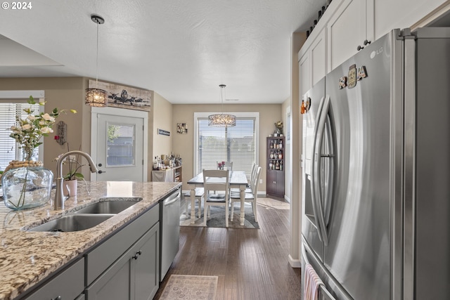 kitchen featuring dark wood-type flooring, sink, light stone counters, hanging light fixtures, and stainless steel appliances