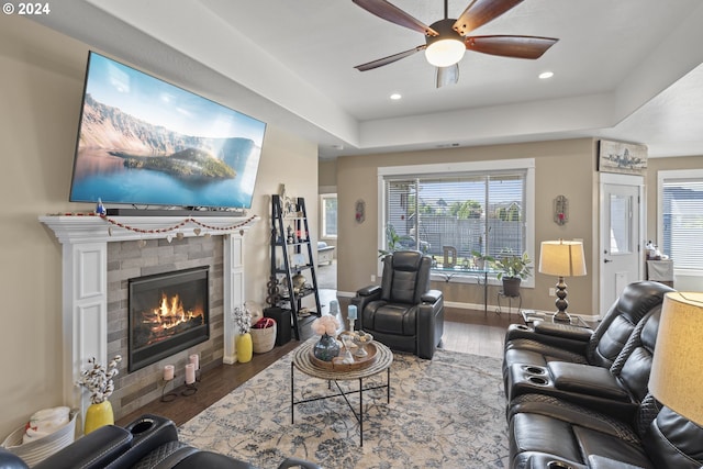 living room featuring a fireplace, a tray ceiling, wood-type flooring, and ceiling fan