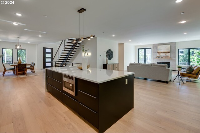 kitchen with a center island, stainless steel microwave, a fireplace, decorative light fixtures, and light hardwood / wood-style floors