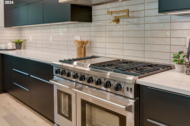 kitchen with light wood-type flooring, decorative backsplash, and high end stove