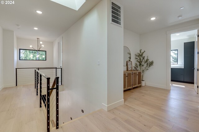 hallway featuring plenty of natural light, a skylight, light wood-type flooring, and a chandelier