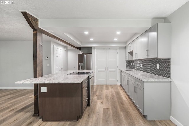 kitchen featuring light wood-type flooring, tasteful backsplash, stainless steel appliances, sink, and a center island