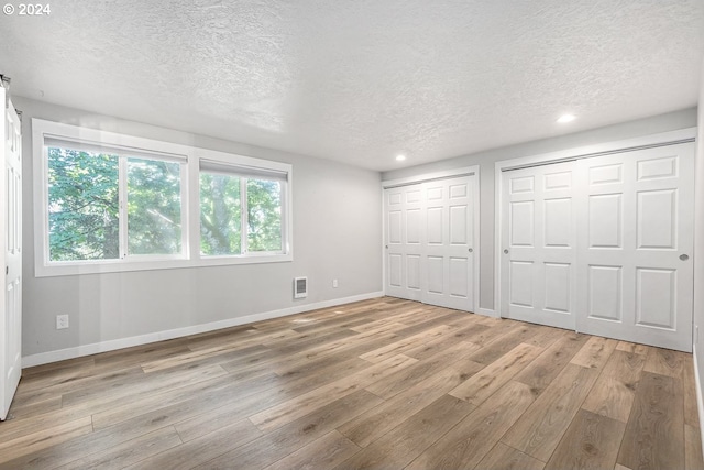 unfurnished bedroom with a textured ceiling, light hardwood / wood-style flooring, multiple windows, and multiple closets