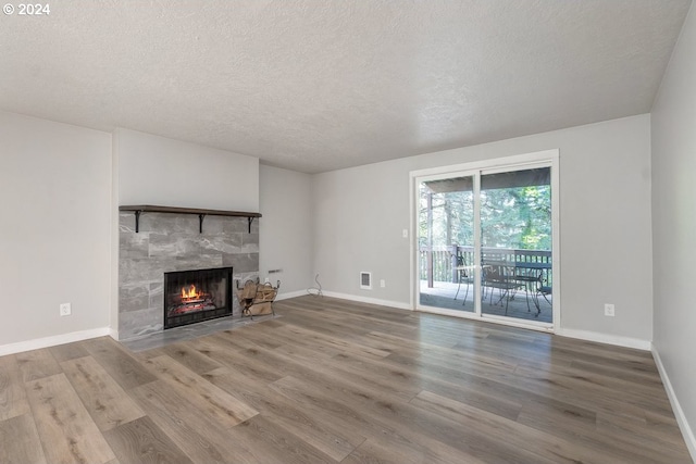 unfurnished living room with a stone fireplace, hardwood / wood-style floors, and a textured ceiling