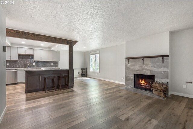 kitchen with dishwasher, open floor plan, a tile fireplace, light wood-style floors, and baseboards