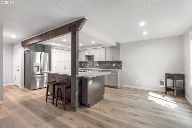 kitchen featuring a kitchen island with sink, light stone countertops, light wood-type flooring, tasteful backsplash, and stainless steel fridge with ice dispenser