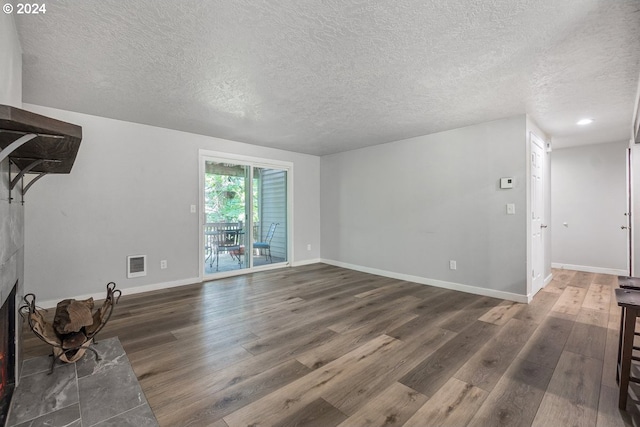 unfurnished living room with wood finished floors, a warm lit fireplace, a textured ceiling, and baseboards