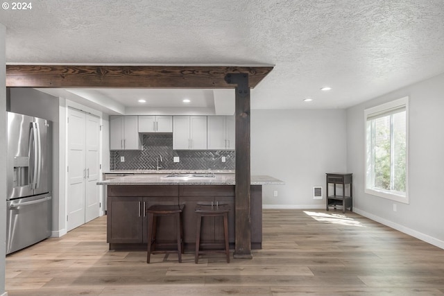 kitchen with a kitchen bar, decorative backsplash, light wood-type flooring, light stone counters, and stainless steel appliances