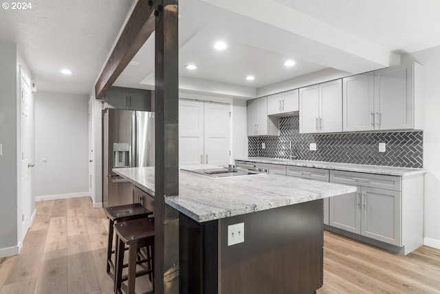 kitchen with gray cabinets, backsplash, light wood finished floors, a breakfast bar, and recessed lighting