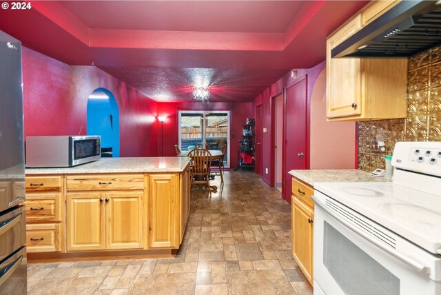 kitchen with appliances with stainless steel finishes, backsplash, a tray ceiling, and exhaust hood