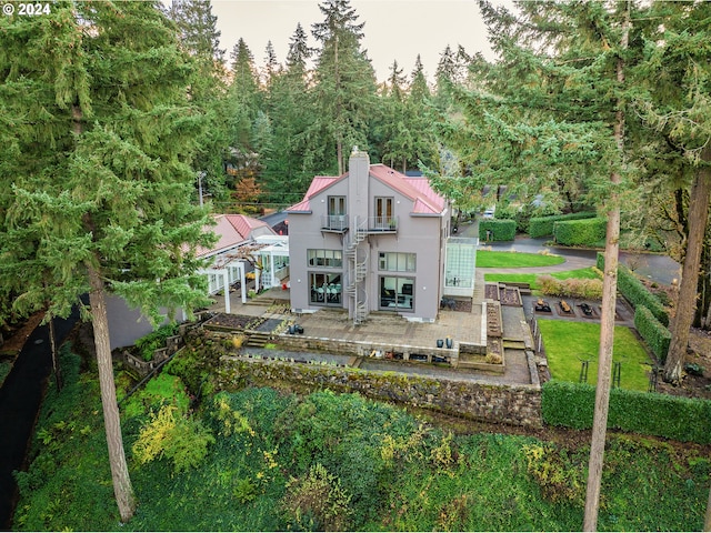 rear view of property featuring a patio area, a balcony, a chimney, metal roof, and stairs