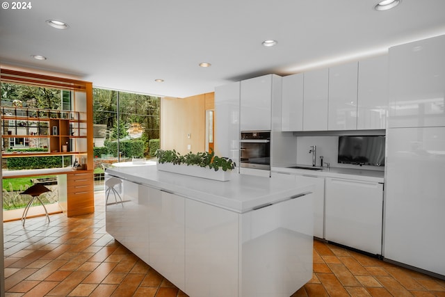 kitchen featuring sink, a wall of windows, white cabinetry, plenty of natural light, and stainless steel oven