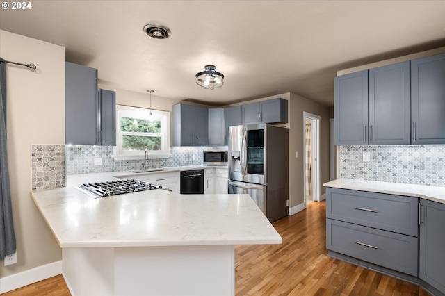 kitchen with sink, kitchen peninsula, stainless steel appliances, and light wood-type flooring