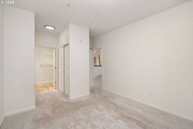 unfurnished living room featuring a tile fireplace, rail lighting, a wall mounted air conditioner, a baseboard heating unit, and light colored carpet