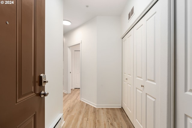 hallway featuring baseboard heating, light wood-style flooring, baseboards, and visible vents