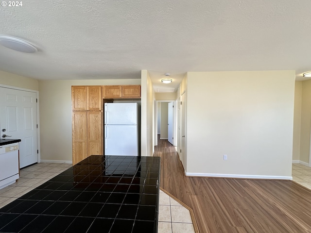 kitchen with tile counters, a textured ceiling, light hardwood / wood-style floors, and white appliances