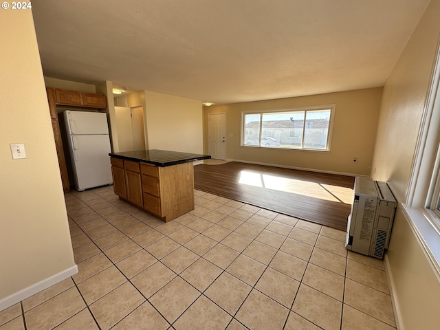 14865 Mt View Dr, Condon, OR 97823 - kitchen with light tile patterned floors, dark countertops, freestanding refrigerator, brown cabinetry, and a kitchen island