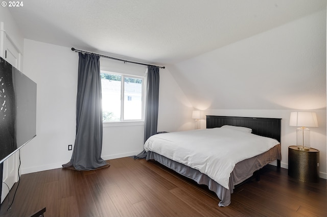 bedroom with a textured ceiling, lofted ceiling, and dark hardwood / wood-style floors