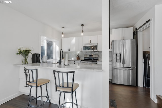 kitchen featuring a barn door, dark wood-type flooring, stainless steel appliances, kitchen peninsula, and white cabinets