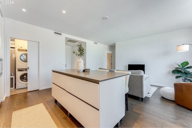 kitchen featuring light hardwood / wood-style floors, stacked washing maching and dryer, a kitchen island, and white cabinets