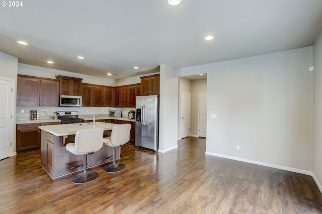 kitchen with appliances with stainless steel finishes, dark hardwood / wood-style flooring, a breakfast bar, and a center island with sink