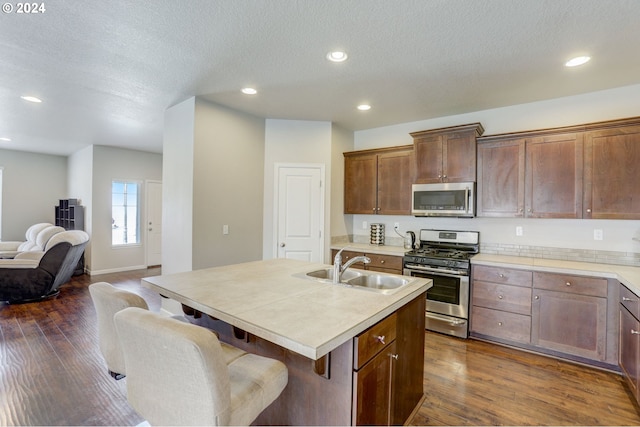 kitchen with dark hardwood / wood-style flooring, stainless steel appliances, sink, a textured ceiling, and an island with sink