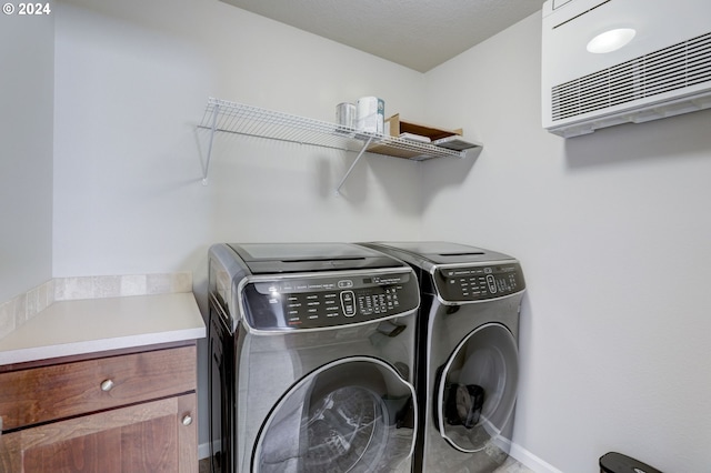 clothes washing area featuring an AC wall unit and washer and clothes dryer