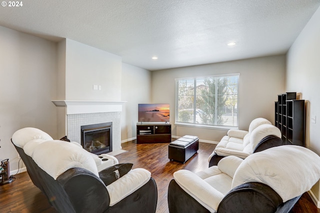 living room featuring a textured ceiling, dark wood-type flooring, and a tile fireplace