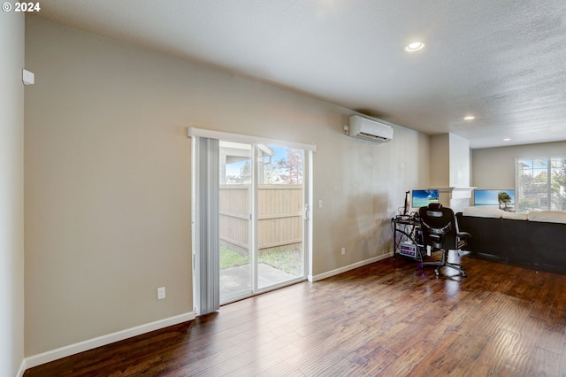 home office with wood-type flooring, a wall unit AC, and a textured ceiling