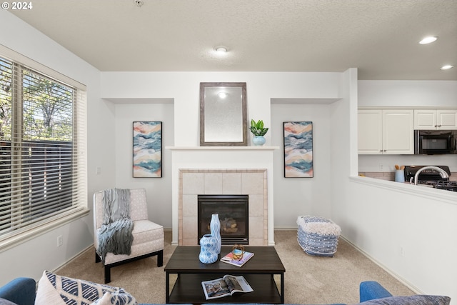 living room with light colored carpet, a textured ceiling, and a tiled fireplace