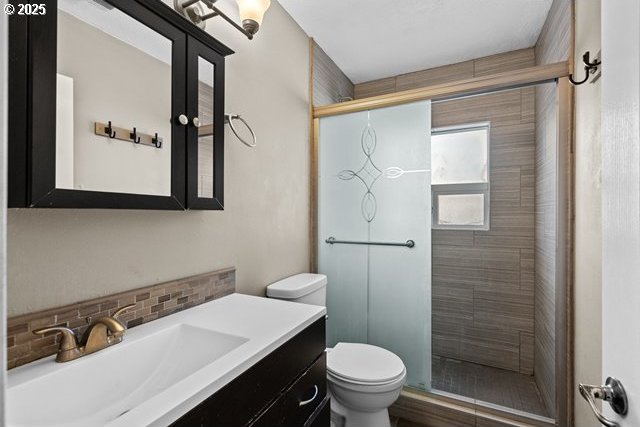 bathroom featuring walk in shower, vanity, toilet, and backsplash