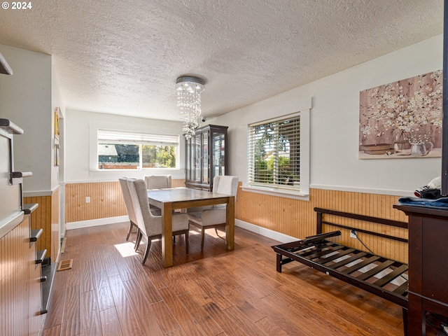 dining area featuring hardwood / wood-style floors, a chandelier, a textured ceiling, and wooden walls