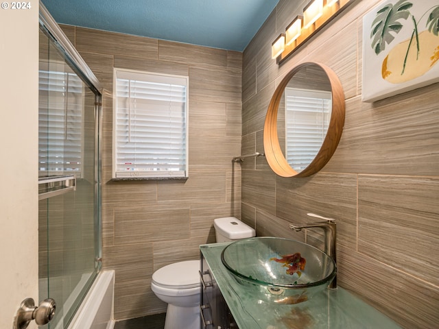 full bathroom featuring a textured ceiling, shower / bath combination with glass door, toilet, tile walls, and vanity