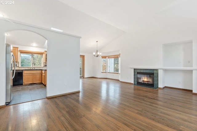 unfurnished living room with a tile fireplace, an inviting chandelier, sink, vaulted ceiling, and dark hardwood / wood-style floors