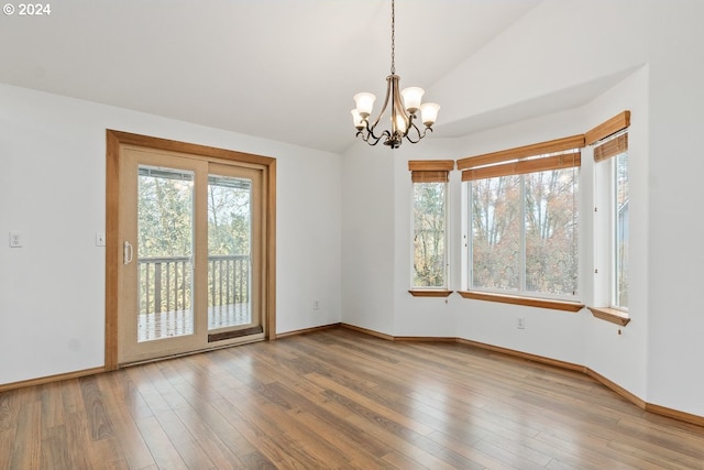 empty room with a notable chandelier, wood-type flooring, and lofted ceiling