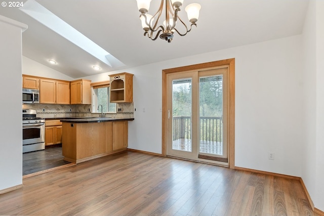 kitchen featuring kitchen peninsula, appliances with stainless steel finishes, vaulted ceiling with skylight, wood-type flooring, and pendant lighting